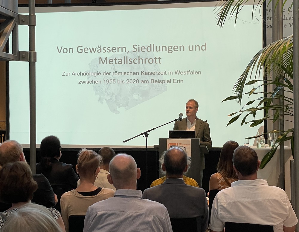 Jona Schröder, junger Mann mit blonden Haaren, hält einen Vortrag vor vielen sitzenden Menschen.